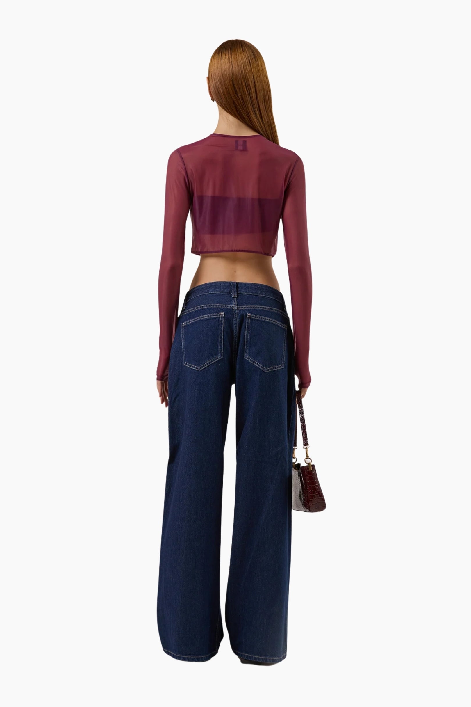 Woman wearing a burgundy long-sleeve top and blue high-waisted jeans on a white background