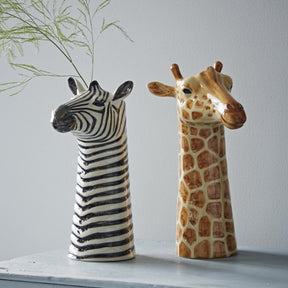 Ceramic zebra and giraffe head vases on a light surface 