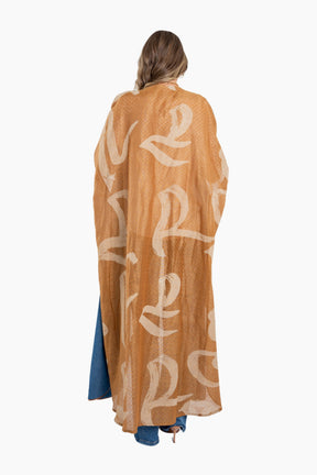 Woman wearing a long, light brown kimono-style garment with white lettering on a white background