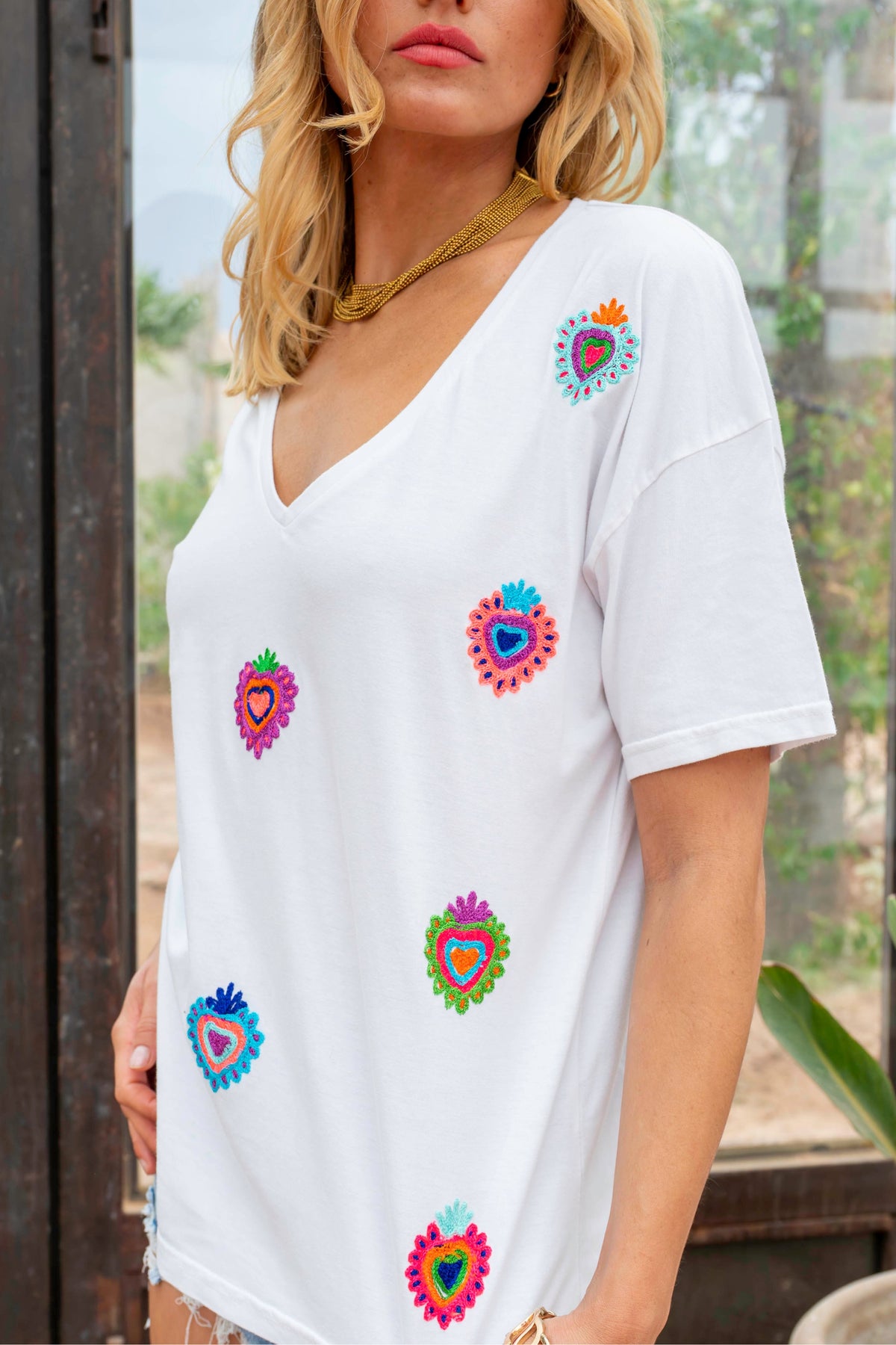 Woman wearing a white t-shirt with colorful heart designs outdoors.