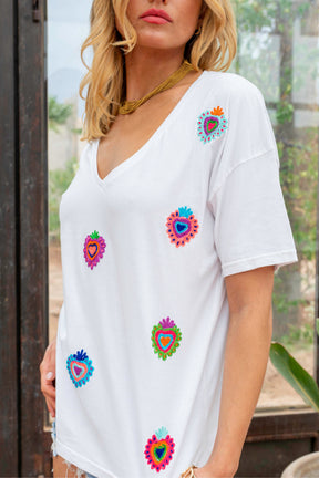 Woman wearing a white t-shirt with colorful heart designs outdoors.