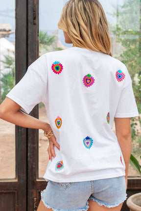 Person wearing a white t-shirt with colorful heart designs outdoors