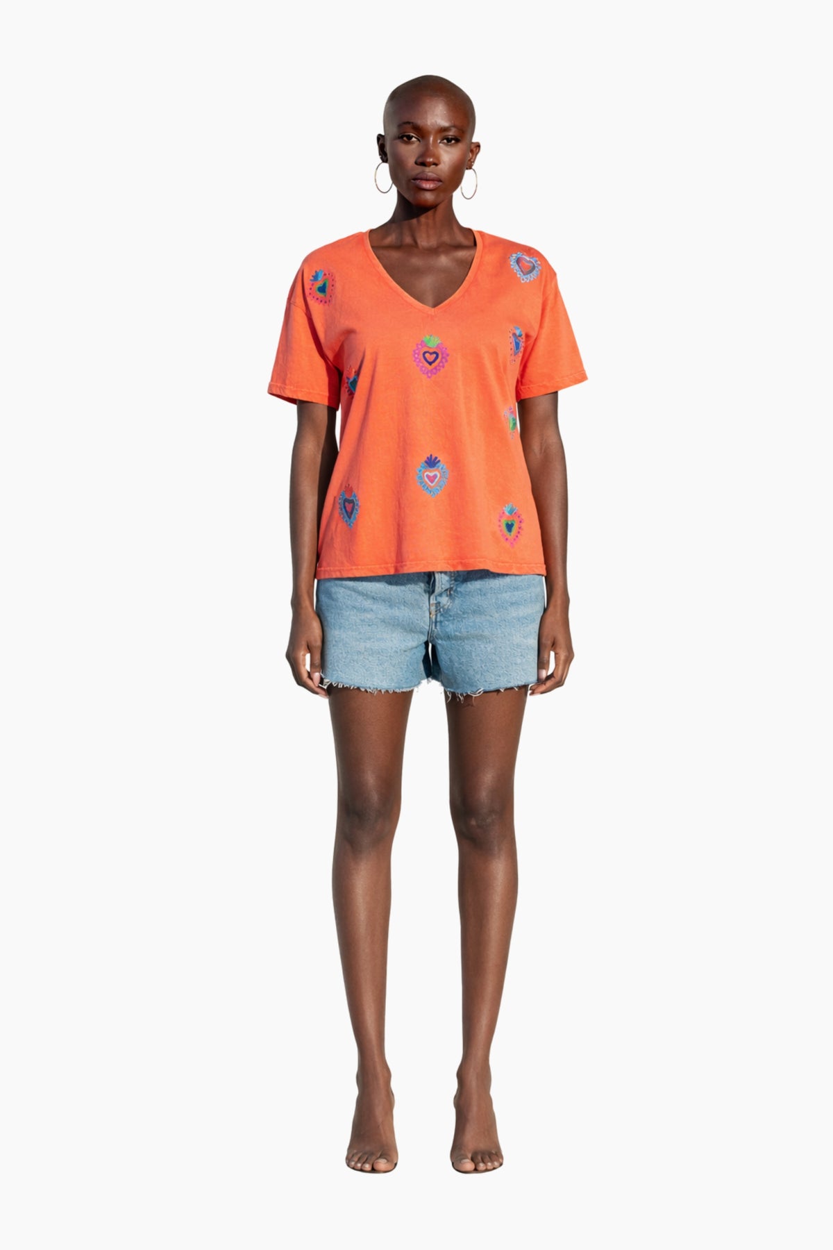 Woman wearing an orange t-shirt with heart patterns and denim shorts on a white background