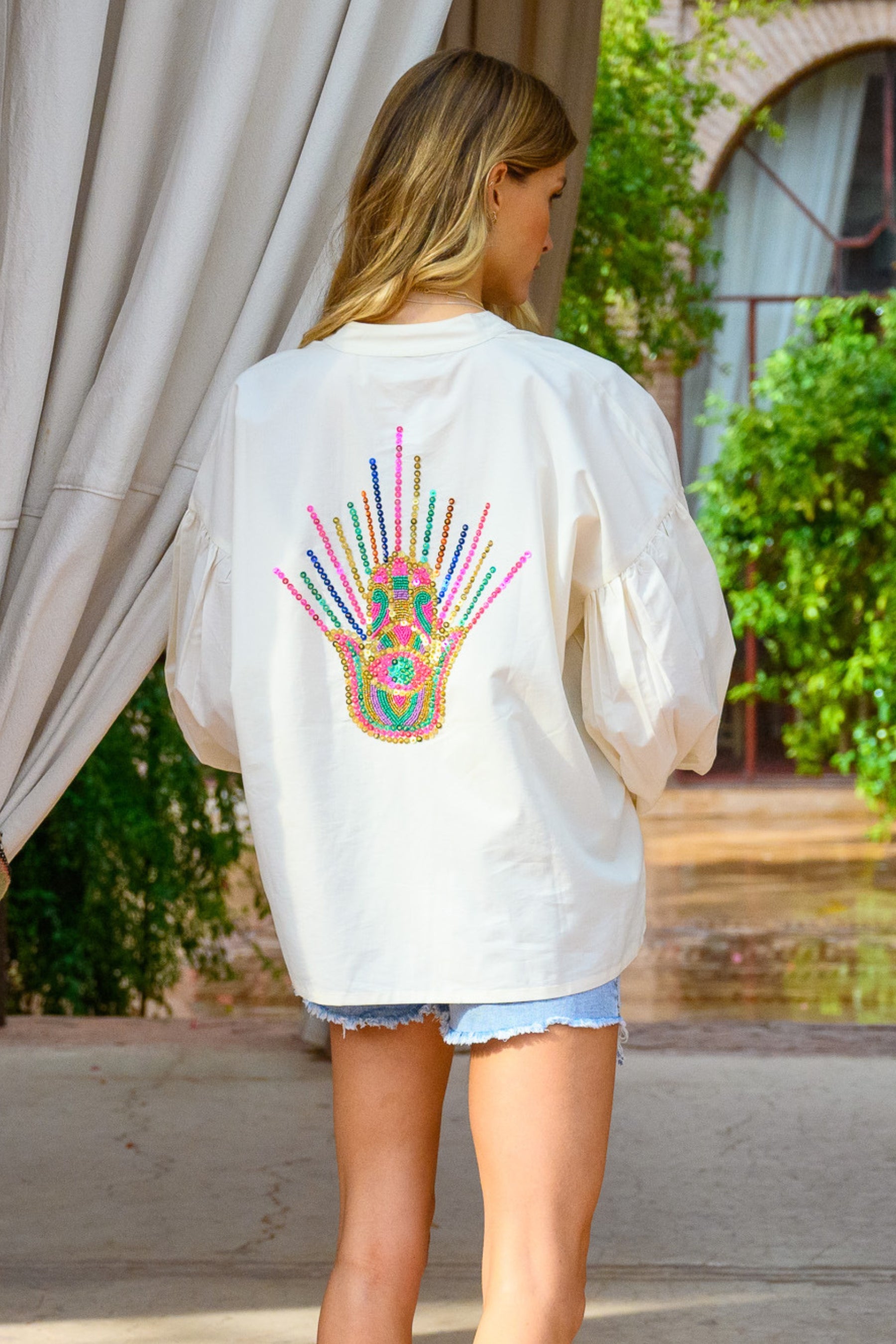 Woman wearing a white sweatshirt with a colorful design on the back, standing outdoors.