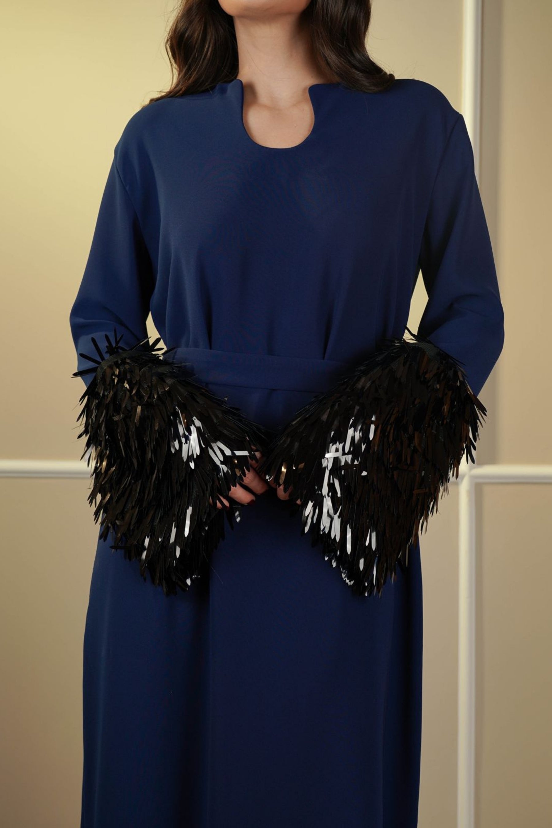Person wearing a blue dress with black feathered gloves against a beige background