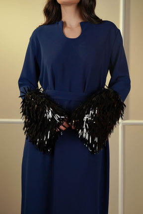 Person wearing a blue dress with black feathered gloves against a beige background