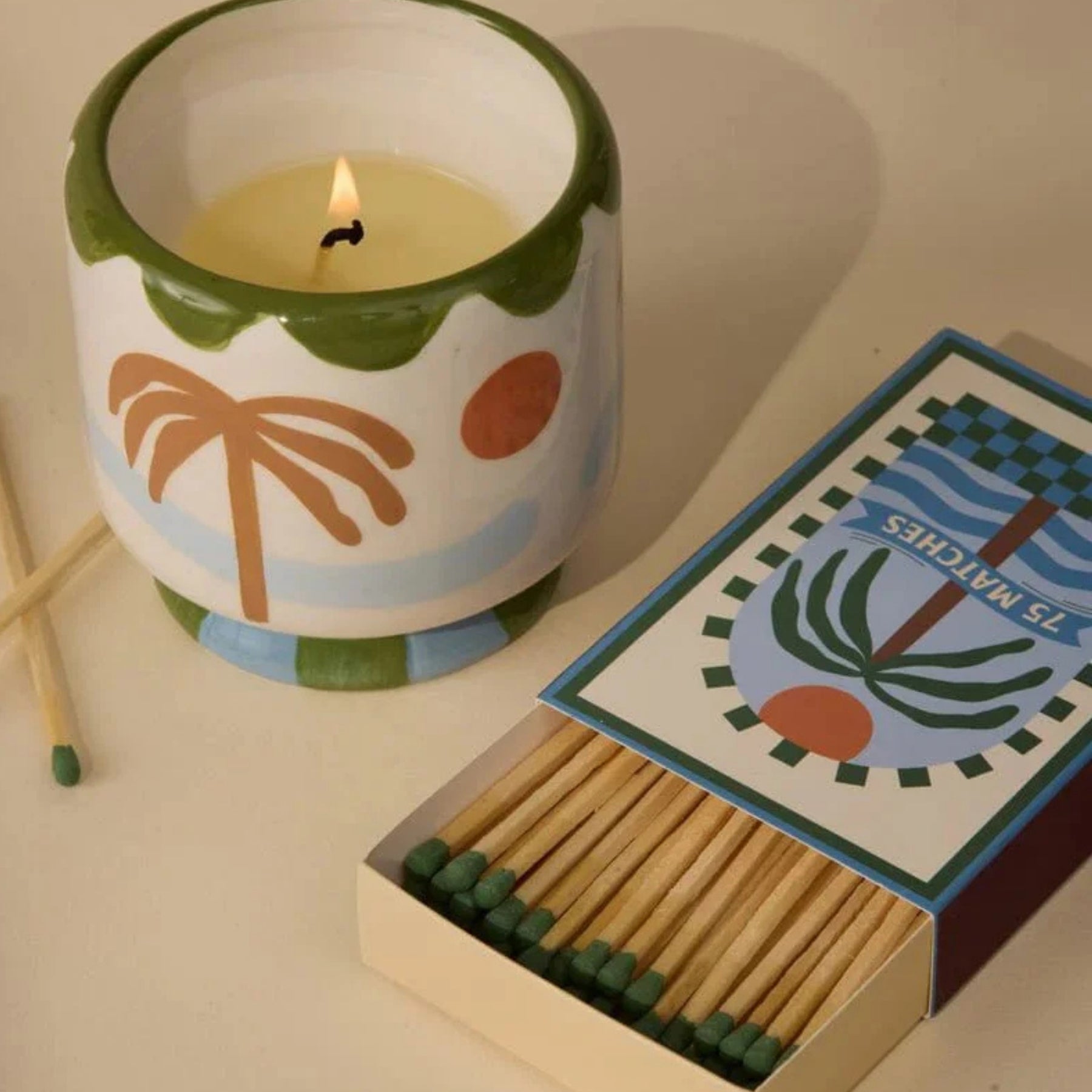 Candle with a decorative design and an open matchbox on a light surface