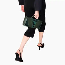 Person wearing a black outfit with a green clutch bag on a white background