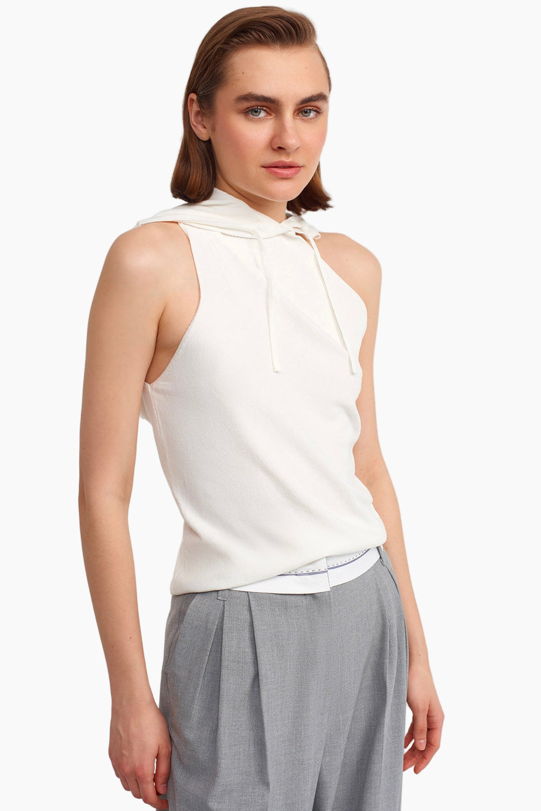 Woman wearing a white sleeveless top with a tie detail and gray pants on a white background