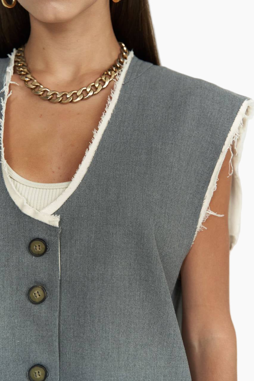Gray vest with button details worn by a person, on a plain background
