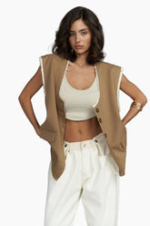 Woman wearing a beige vest over a white top and pants on a white background