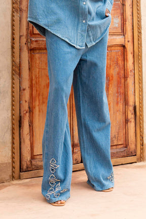 Person wearing blue jeans with floral embroidery in front of a wooden door.