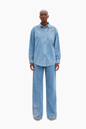 Person wearing a blue denim outfit with embroidery on a white background
