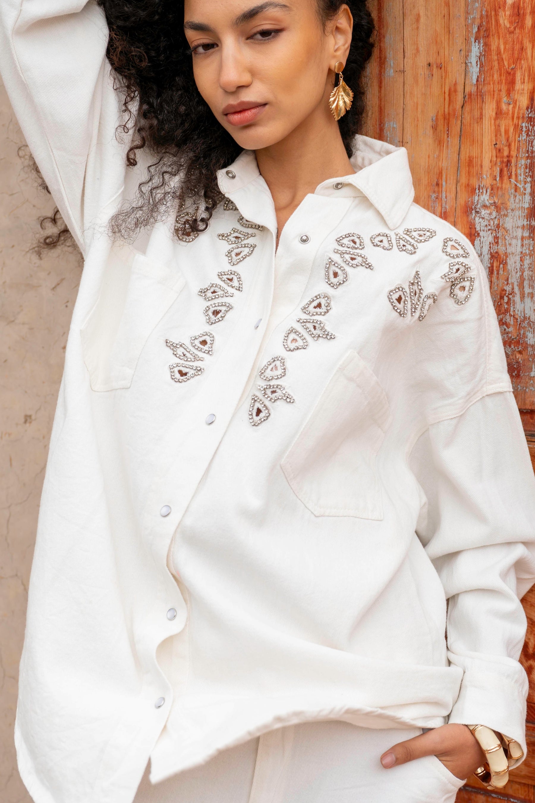 Woman wearing a white embroidered blouse against a wooden wall.