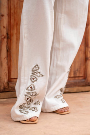 White pants with intricate silver embroidery on a wooden floor.