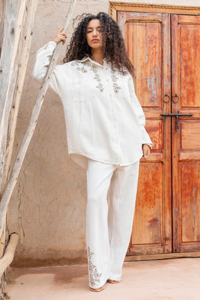 Woman in a white embroidered outfit standing in front of a wooden door.