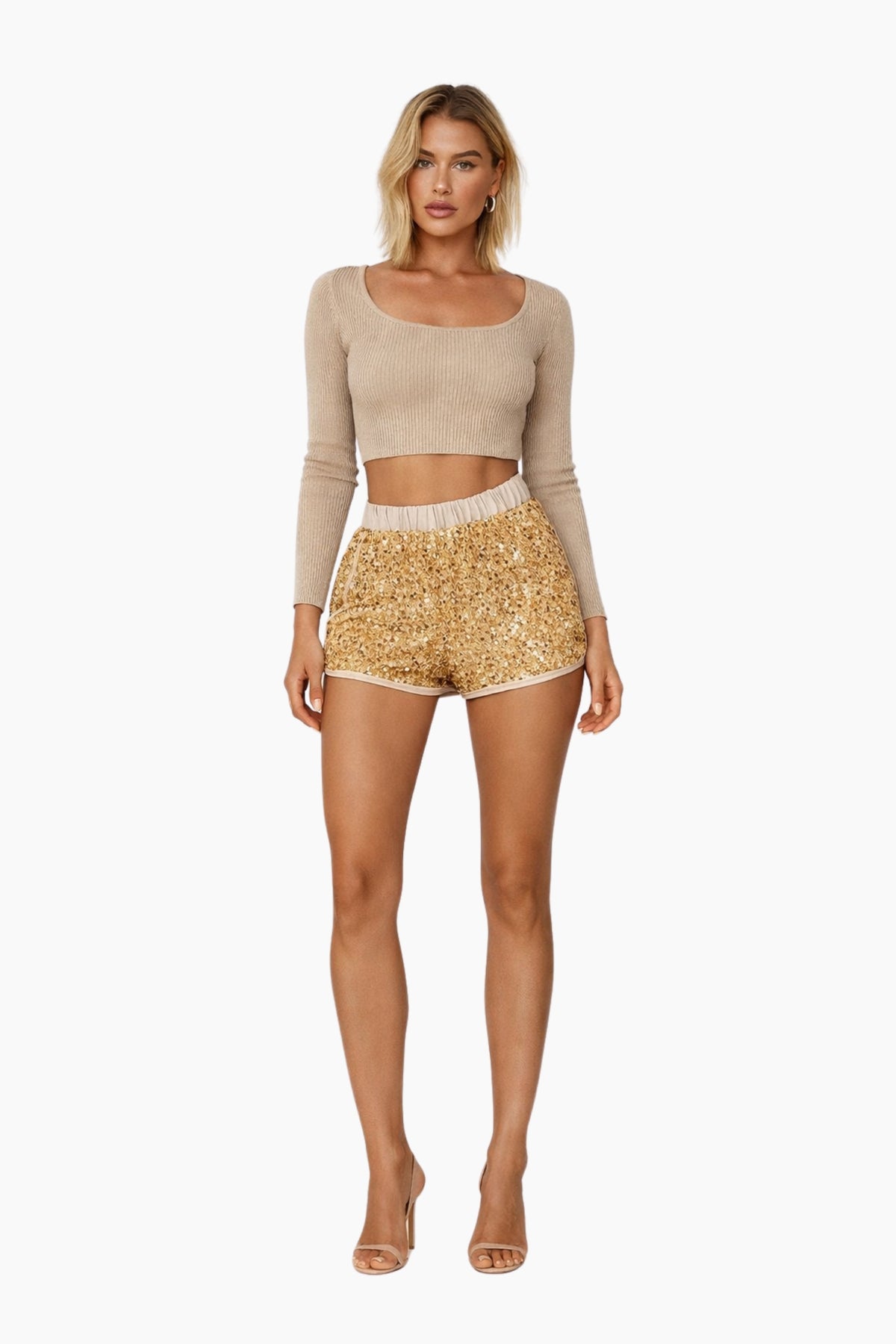 Woman wearing a beige long-sleeve top and gold sequin shorts on a white background