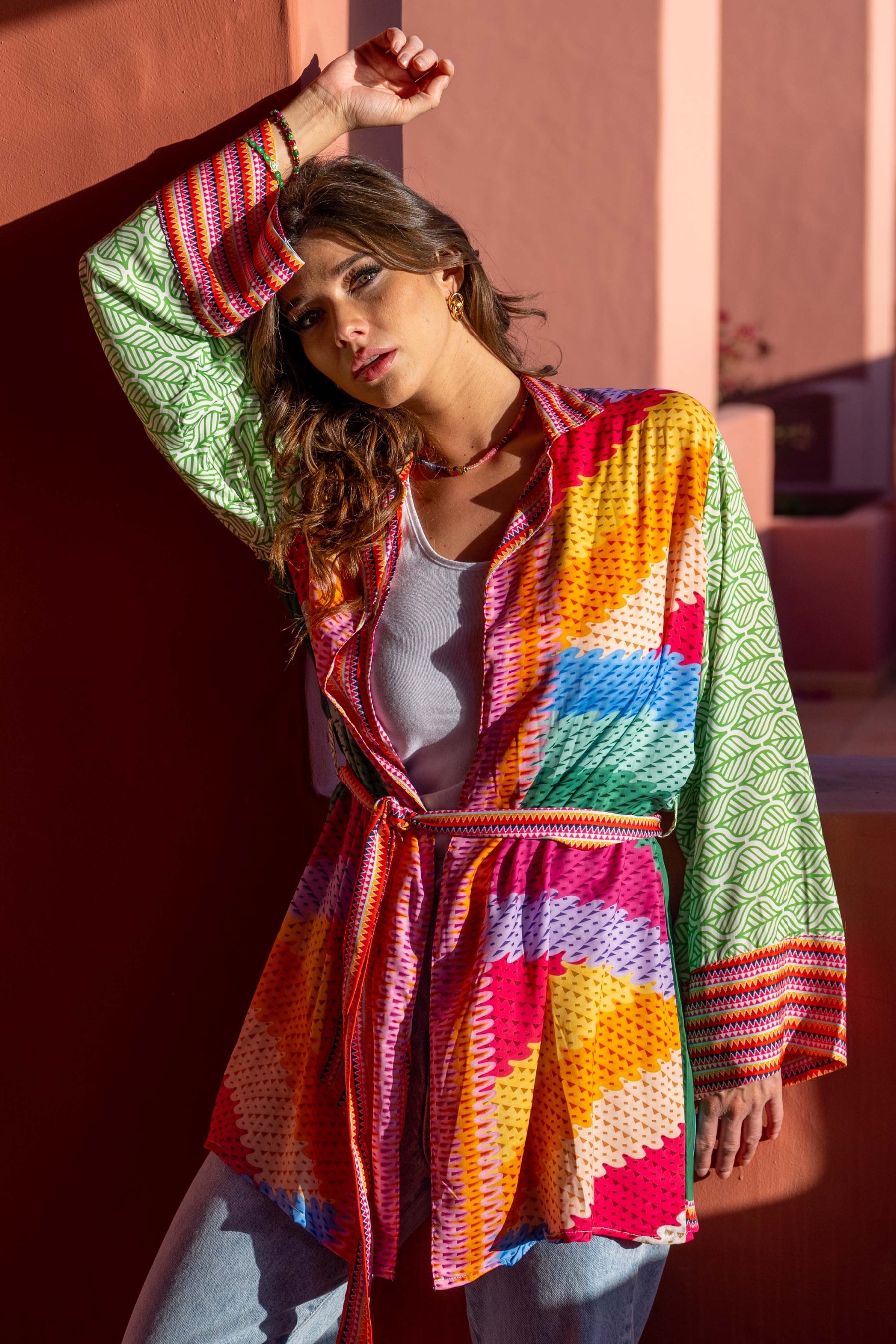 Woman wearing a colorful, patterned jacket against a warm-toned wall.