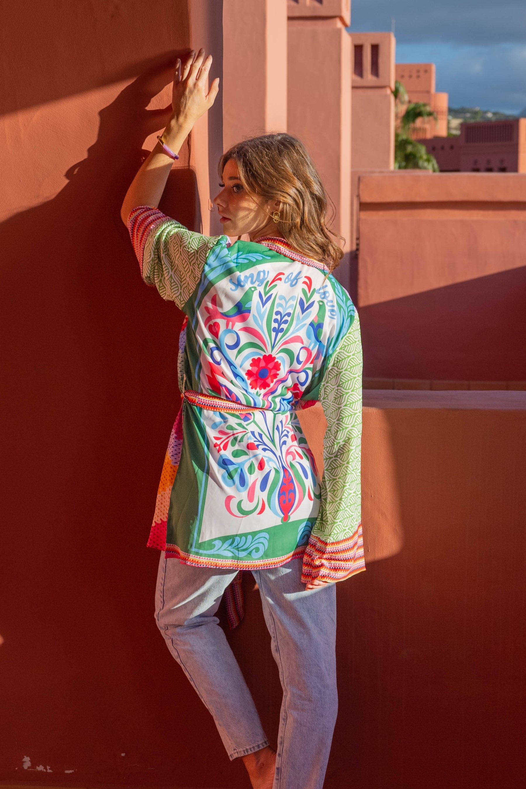 Woman wearing a colorful patterned jacket against a red wall.