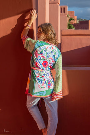 Woman wearing a colorful patterned jacket against a red wall.