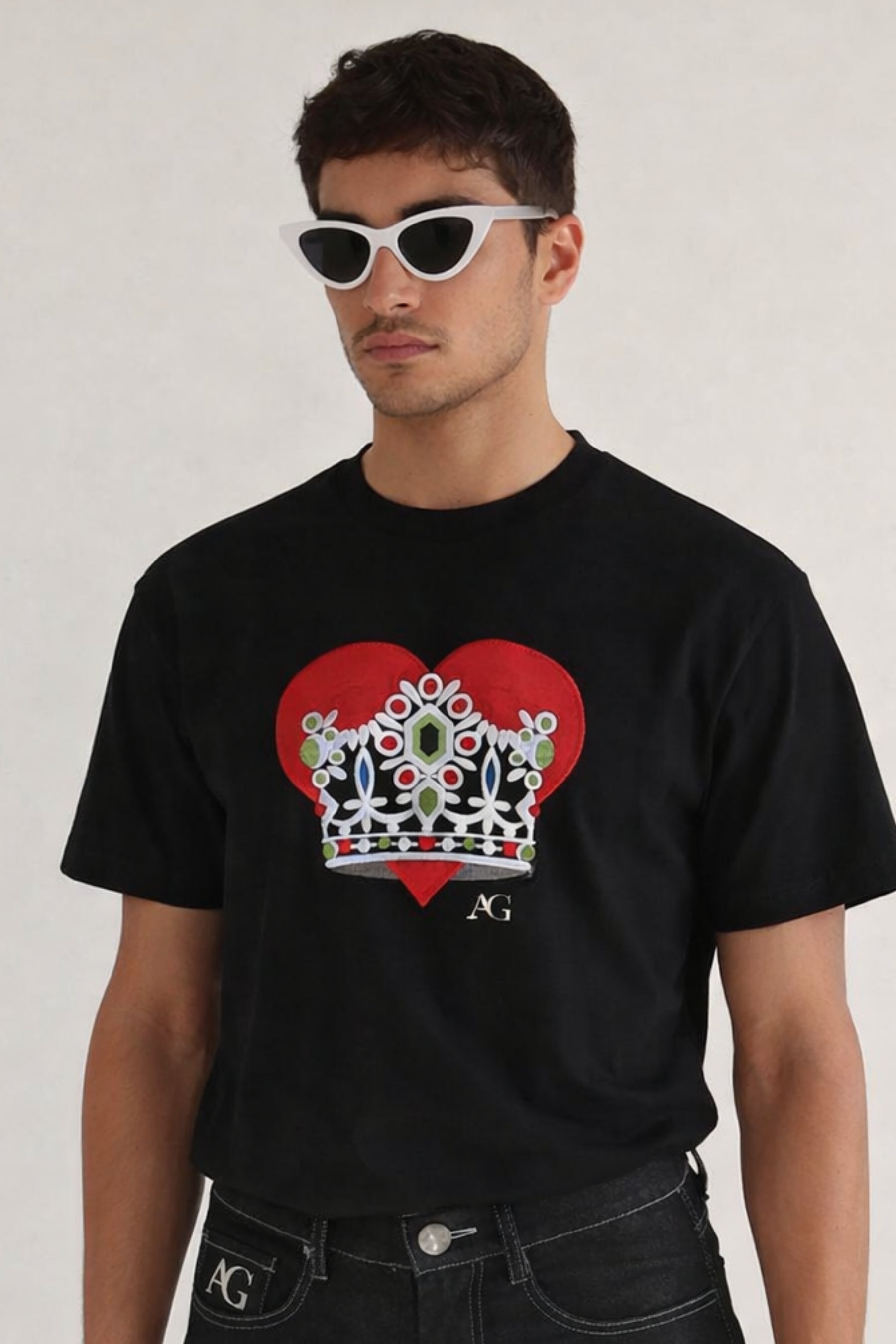 Man wearing a black t-shirt with a red heart and crown design on a plain background
