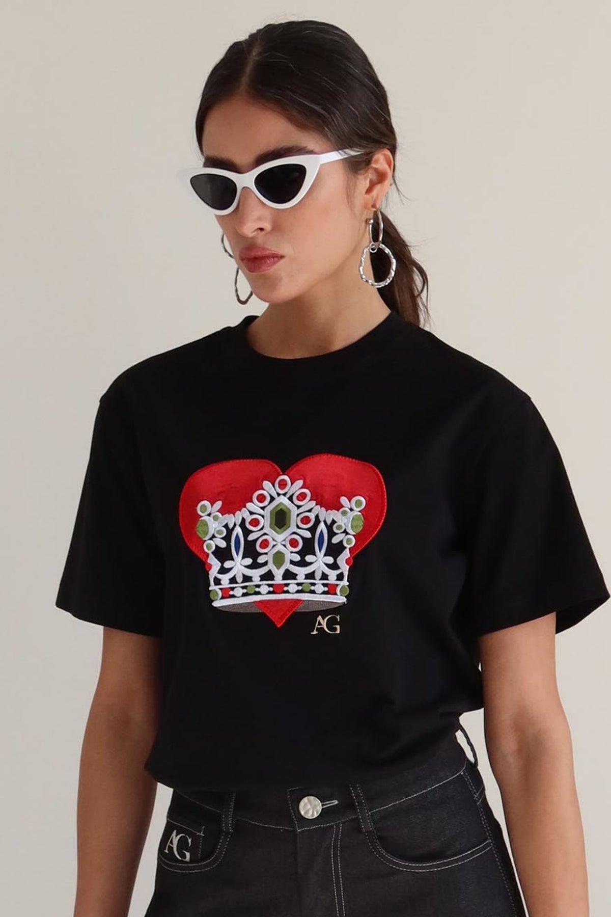 Person wearing a black t-shirt with a red heart and crown design, standing against a plain background.