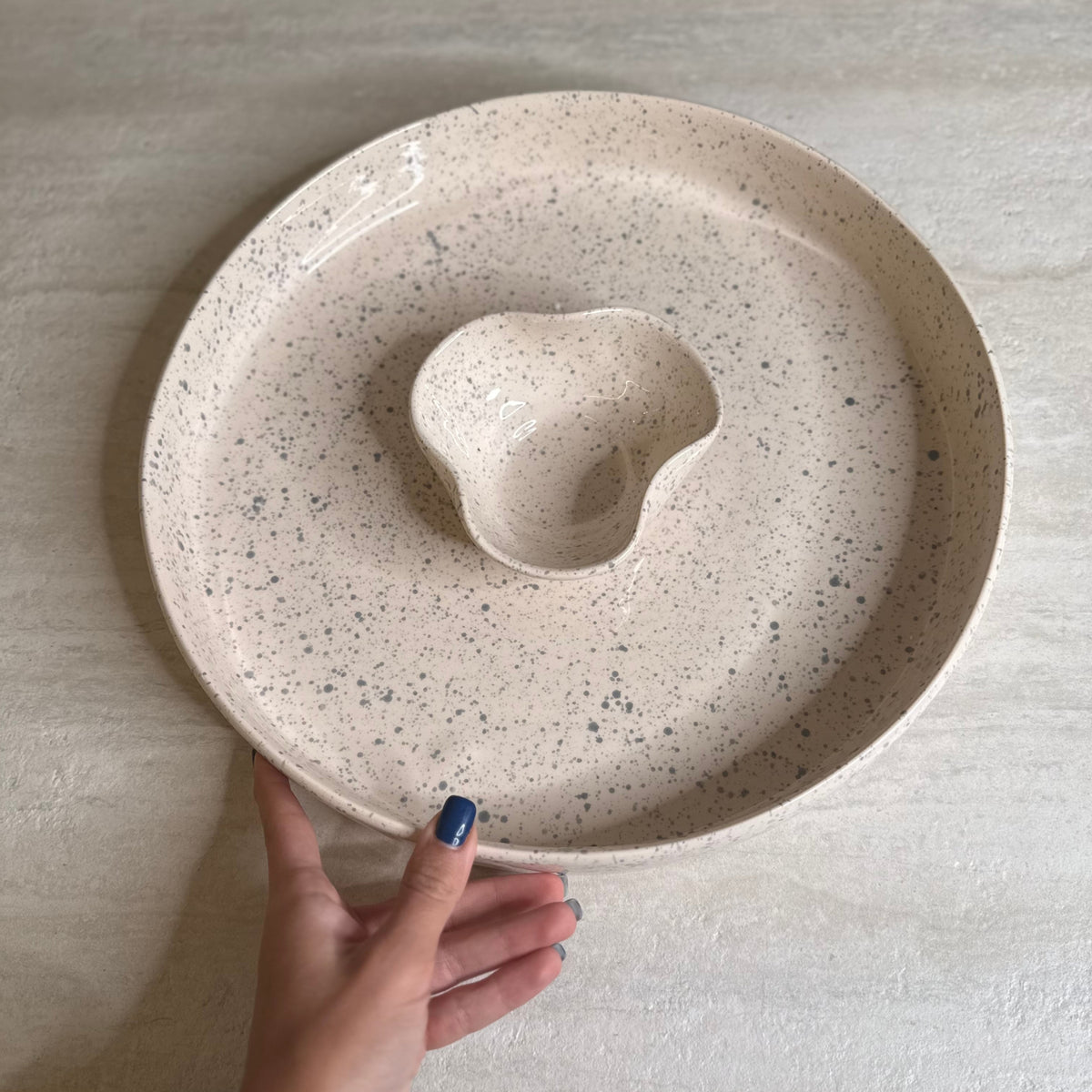 Hand holding a speckled ceramic plate with a central raised stone-like object