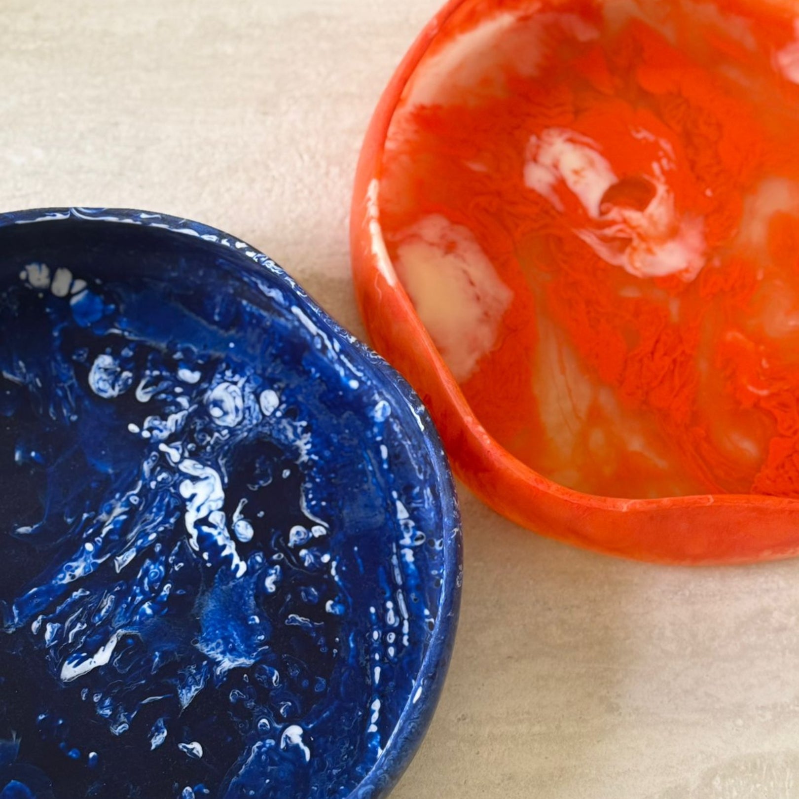 Two ceramic bowls, one blue and one red, on a beige surface.