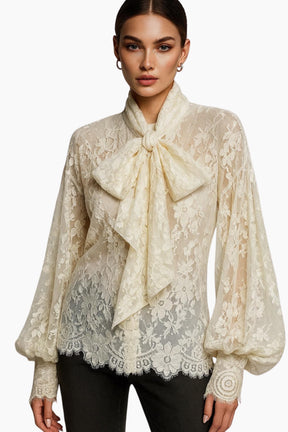 Woman wearing a beige lace blouse with a large bow tie on a white background