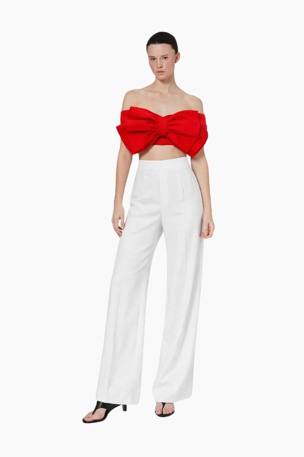 Model wearing a red strapless top with a large bow and white pants on a white background
