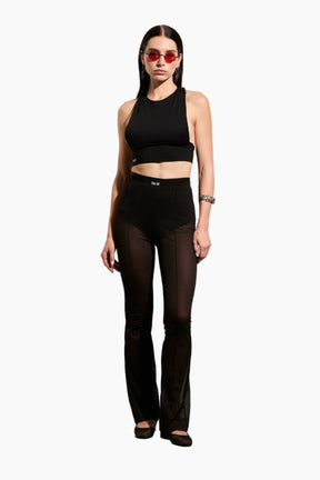 Woman wearing a black sleeveless top and mesh black pants 