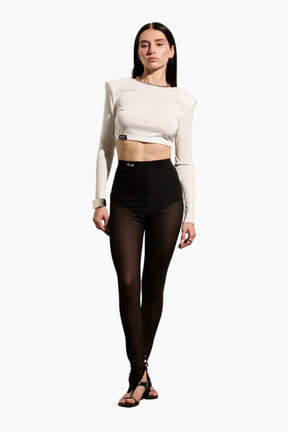 Woman wearing a beige long-sleeve crop top and black Mesh leggings with metal buttons at the ankle.